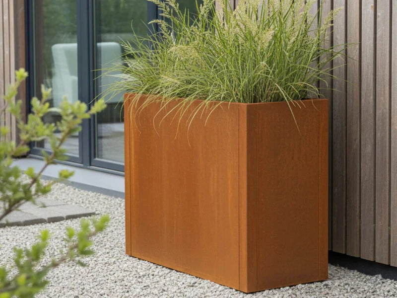 Hög blomlåda i cortenstål från CUBY med prydnadsgräs vid fasad