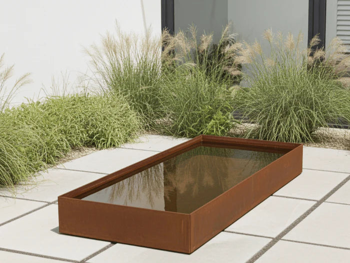 Rektangulart vattenkar i cortenstål som modern vattenspegel i trädgård
