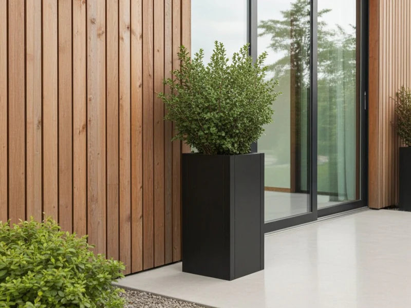 Blomkruka i svart stål med buske vid terrass