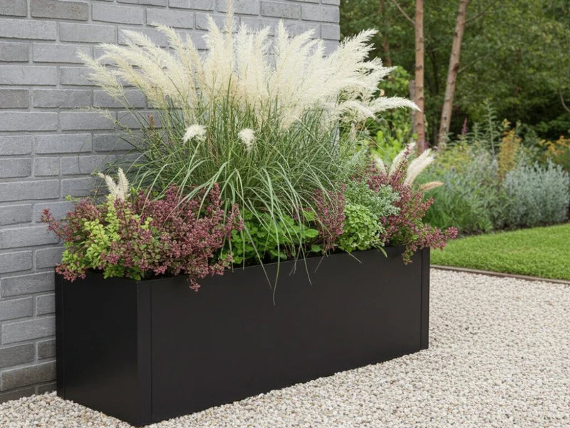 Blomlåda i svart stål med prydnadsgräs i grusplantering