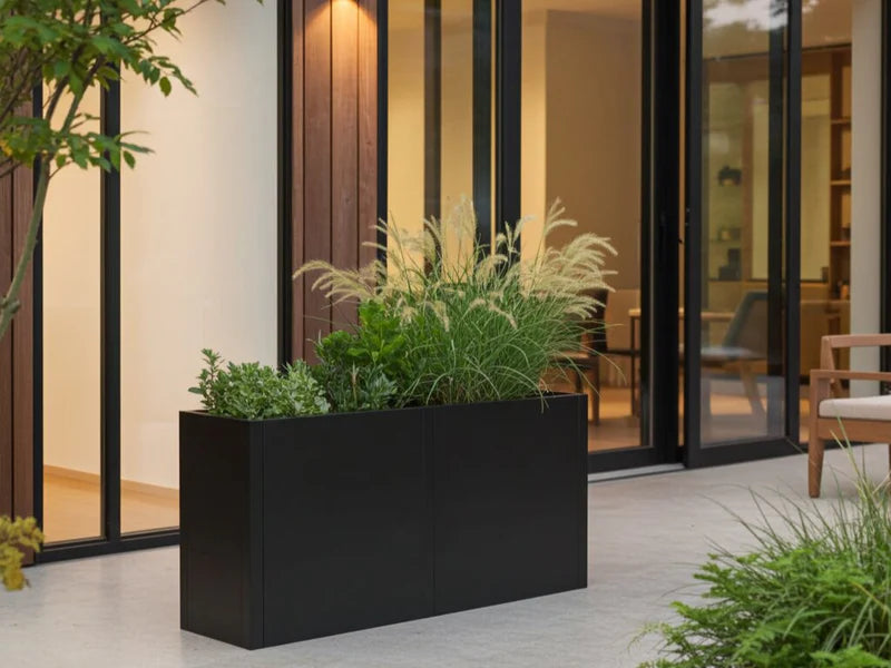 Blomlåda i svart stål med prydnadsgräs vid modern terrass