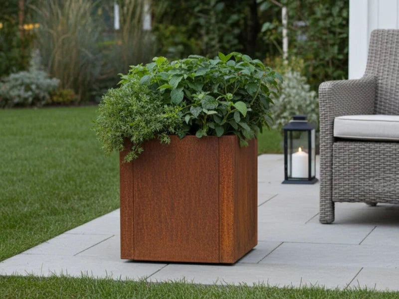 CUBY blomlåda i cortenstål med frodig plantering i trädgård