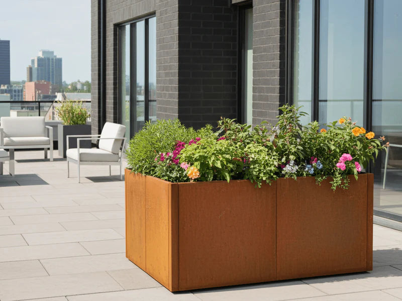 Stor blomlåda i cortenstål från CUBY med färgglada blommor på terrass