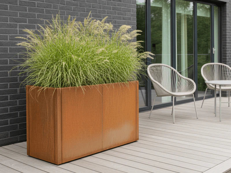 Blomlåda i cortenstål från CUBY fylld med grönska på träterrass
