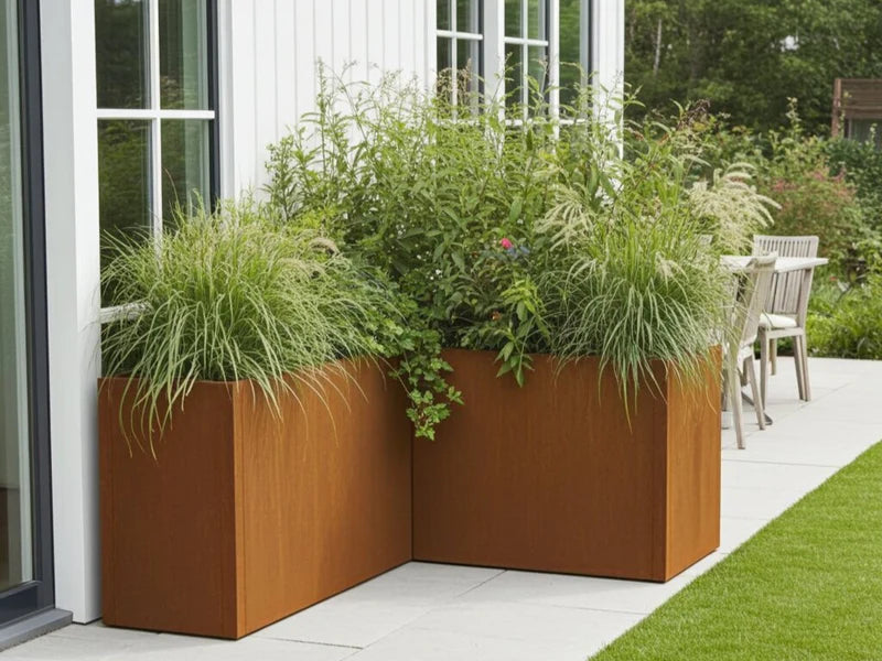 Blomlåda i cortenstål från CUBY placerad som hörnplantering vid fasad