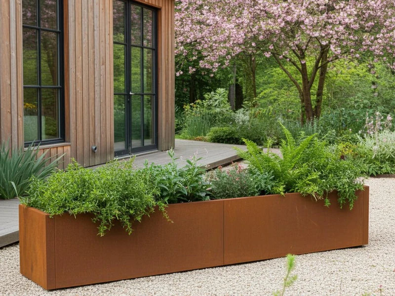 Lång blomlåda i cortenstål från CUBY med perenner framför modernt hus