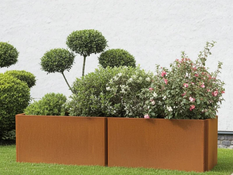 EDGY blomlåda i cortenstål med blommande buskar och grön plantering