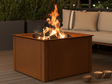 Fyrkantig eldstad i cortenstål på terrass med loungemöbler och levande eld i kvällsmiljö