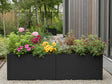 Lång blomlåda i svart stål med blommande växter i modern trädgård