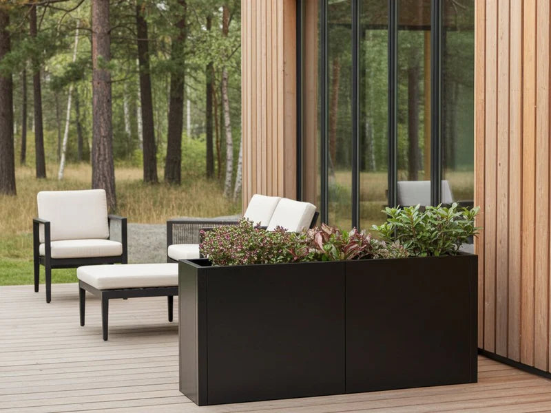 Lång blomlåda i svart stål med perenner vid terrass